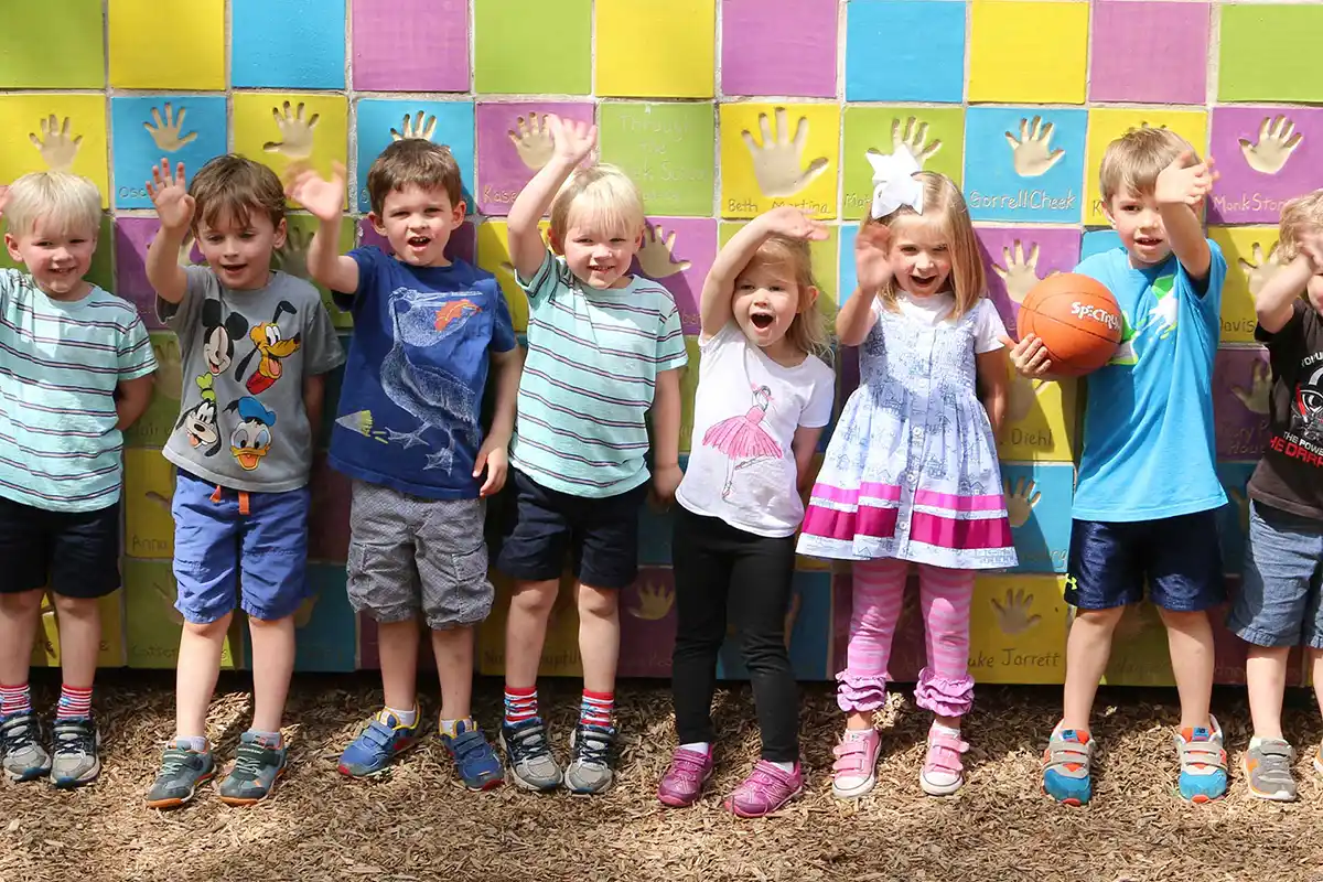 Preschool teacher and children playing together in the grass with a playground in the background